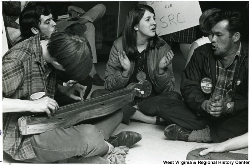 Students sitting on the ground, one playing a dulcimer