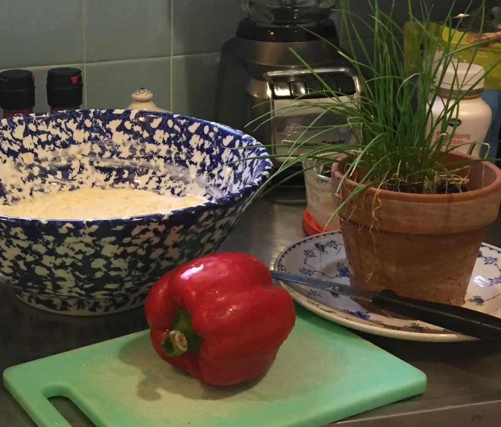 Image of food preparation showing red bell pepper, chives plant, and mixing bowl