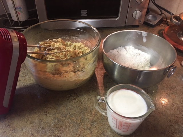 Mixing bowl of flour, mixing bowl of batter with electric handmixer, and cup of milk