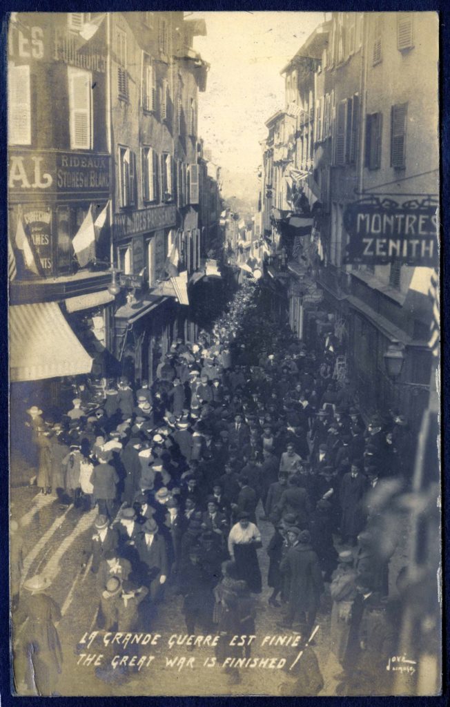 Postcard showing a crowd of people filling a French city street, with the text in English and French, "The Great War is Finished!"