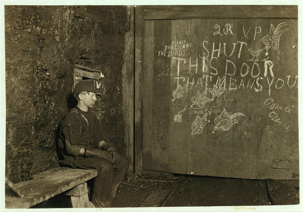 Boy sitting in front of a mine door with writing and images on it