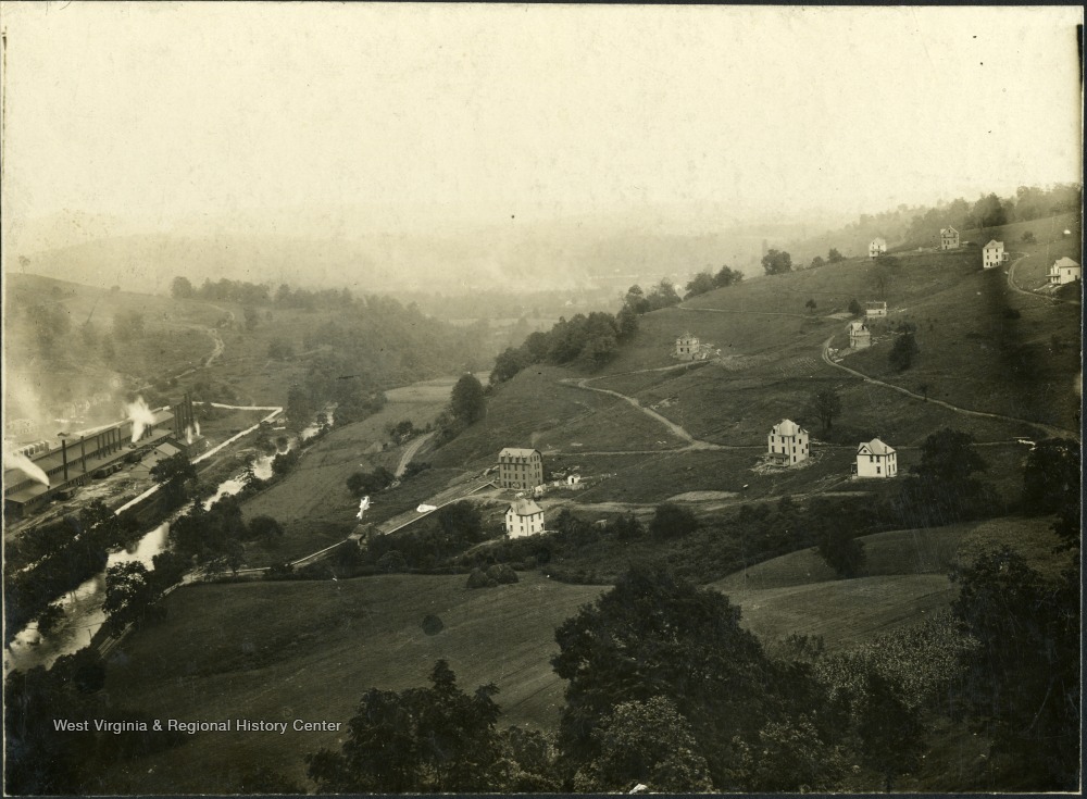 Image of hillsides dotted with a few houses, and a factory at the bottom.