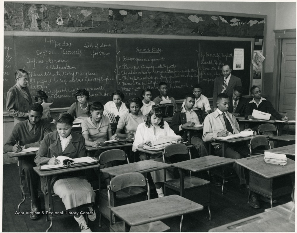 Students seated at desks in a classroom as teachers look on