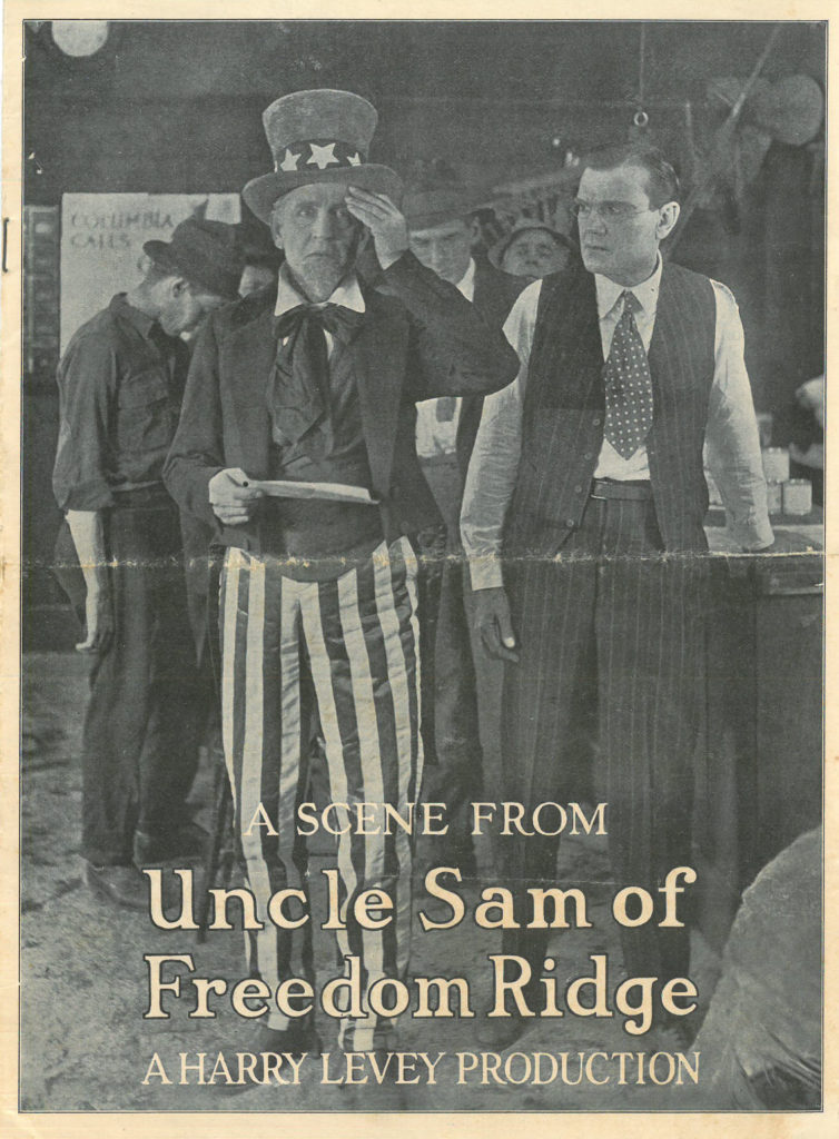 Image of a man dressed as Uncle Sam holding a piece of paper, as another man in vest and tie looks on. Text says "A Scene from Uncle Sam of Freedom Ridge A Harry Levey Production"