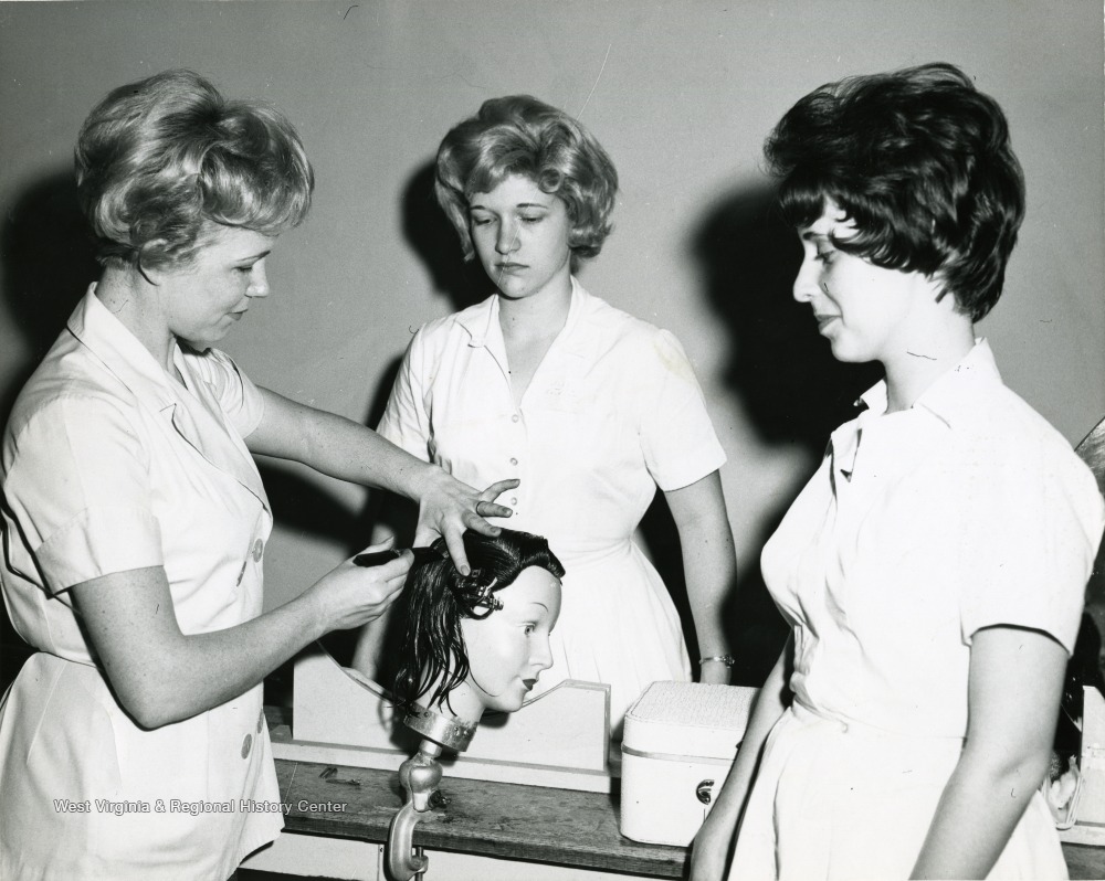 Female student dresses the hair of a mannequin as two others look on.