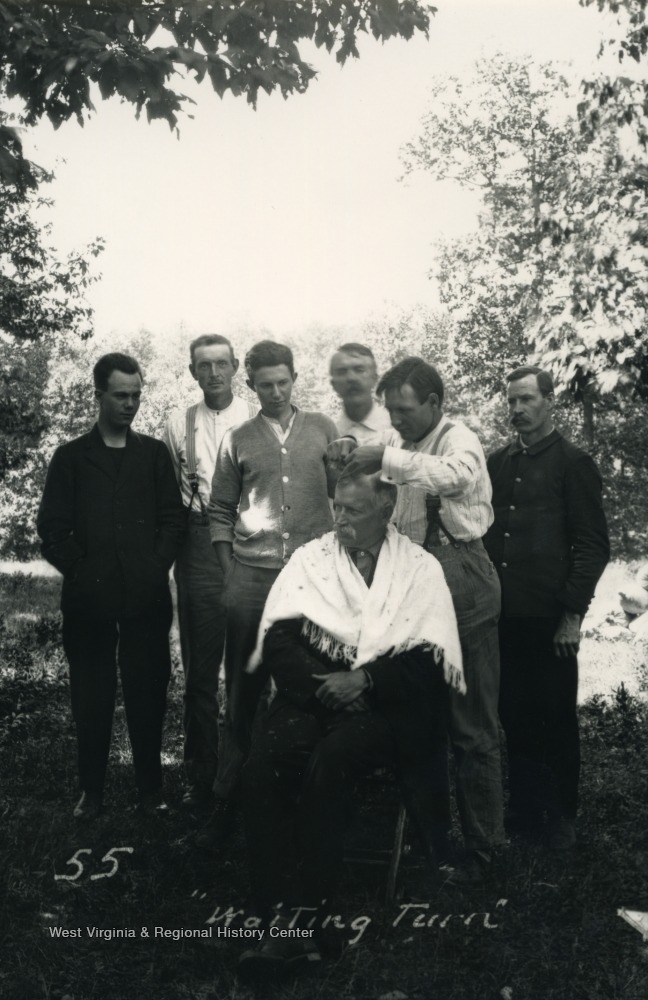 Man receiving a haircut outdoors while other men look on