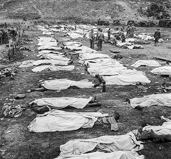 Photo of bodies laid out in rows and covered in white sheets, while a few people mill around