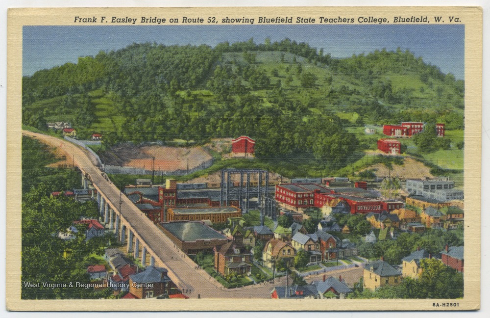 Buildings with a road on the left and wooded hills in the background