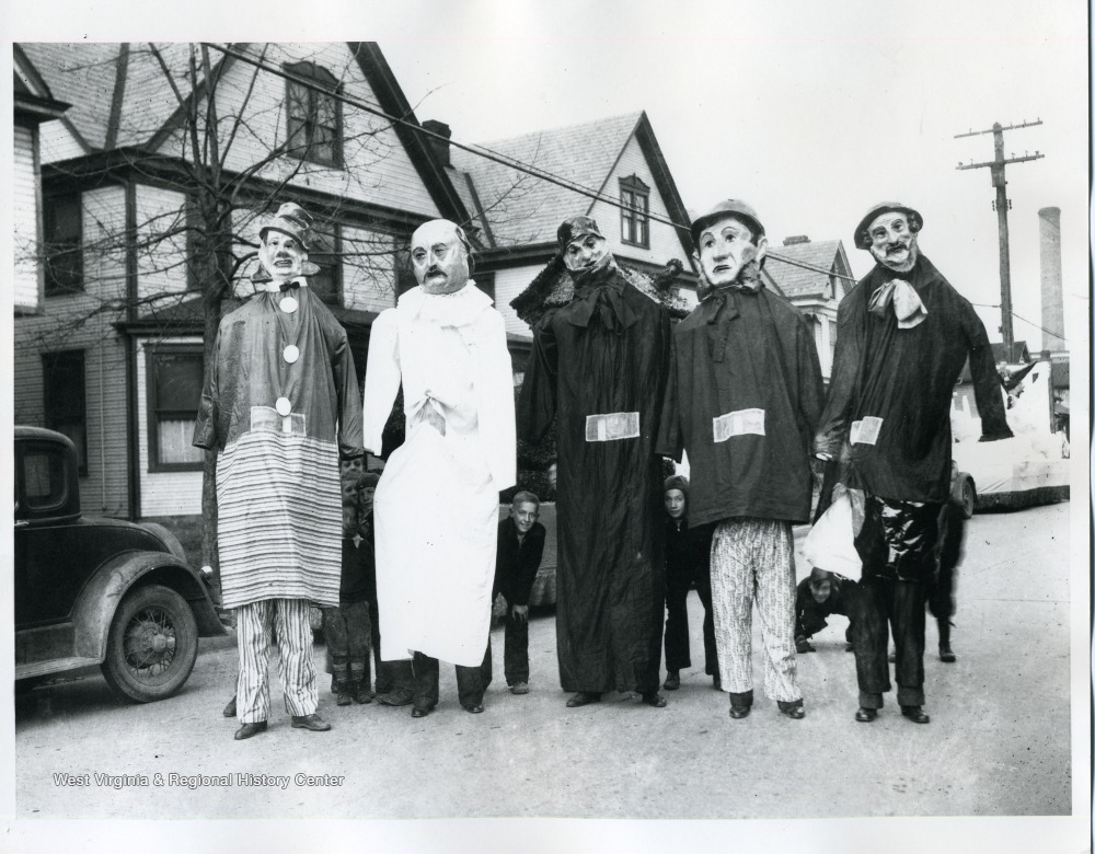 Children hiding behind five people in very tall person costumes.