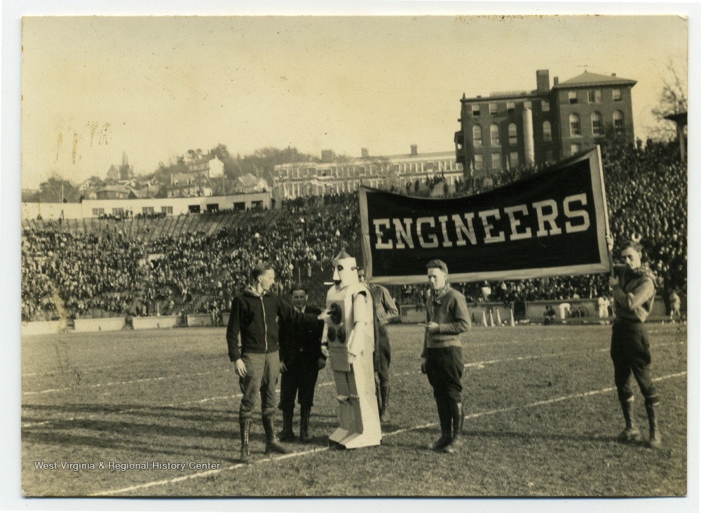 Men on stadium field holding "Engineers" sign, with man in robot costume.