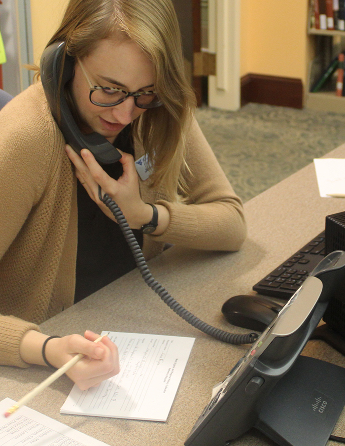 Woman on telephone, writing on a pad of paper.