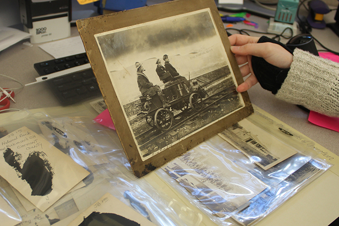 Mounted photo of men on a small train car, held atop other photos on a table.