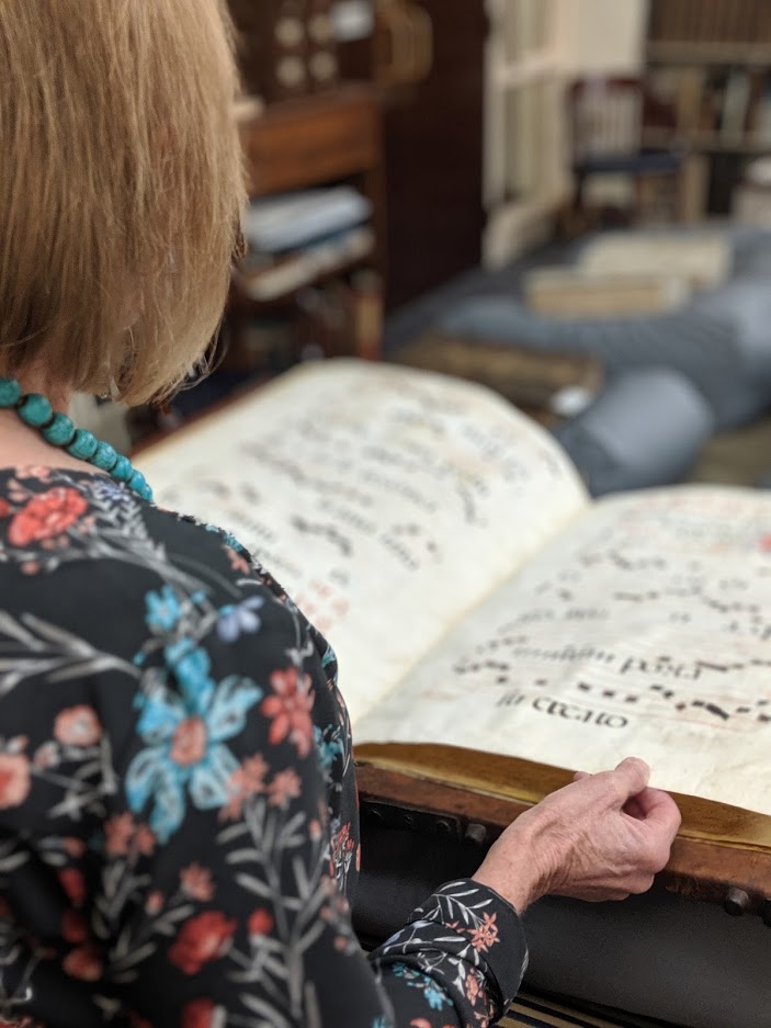 Woman turning the page of an old oversize book full of musical notation.