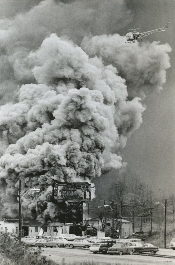 Huge plume of smoke billowing from an obscured structure over a parking lot