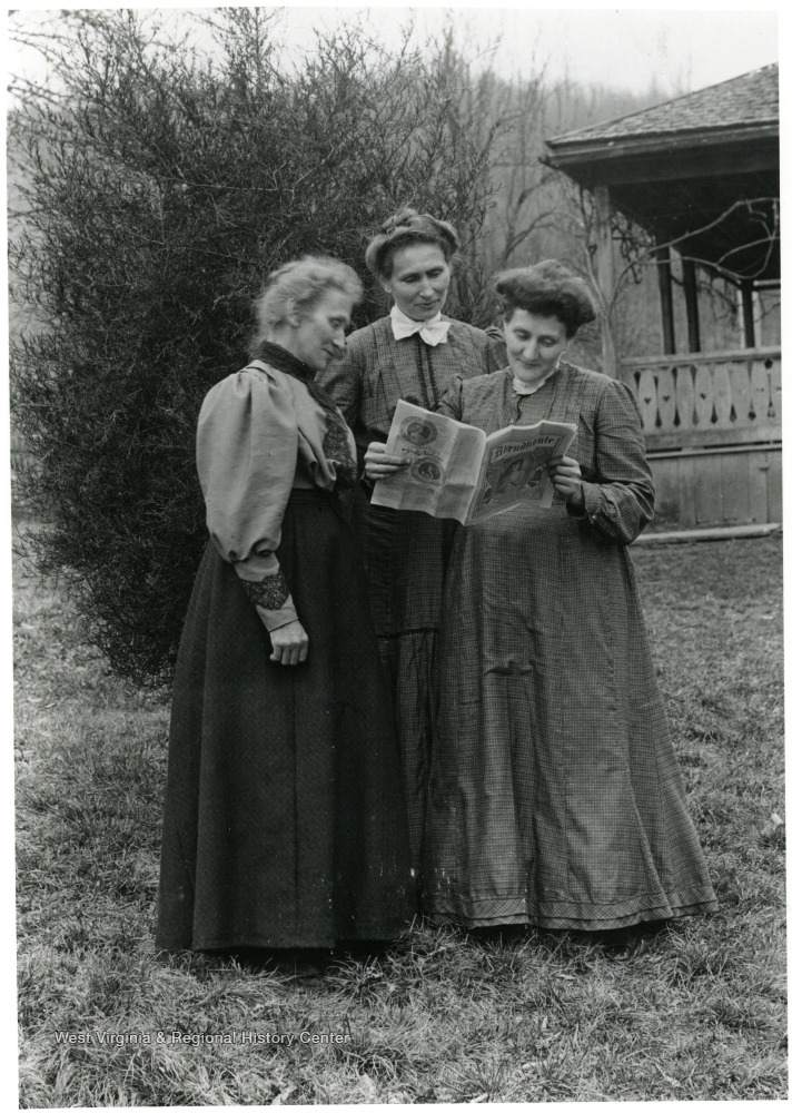 Photo of three women standing outdoors around a newspaper.