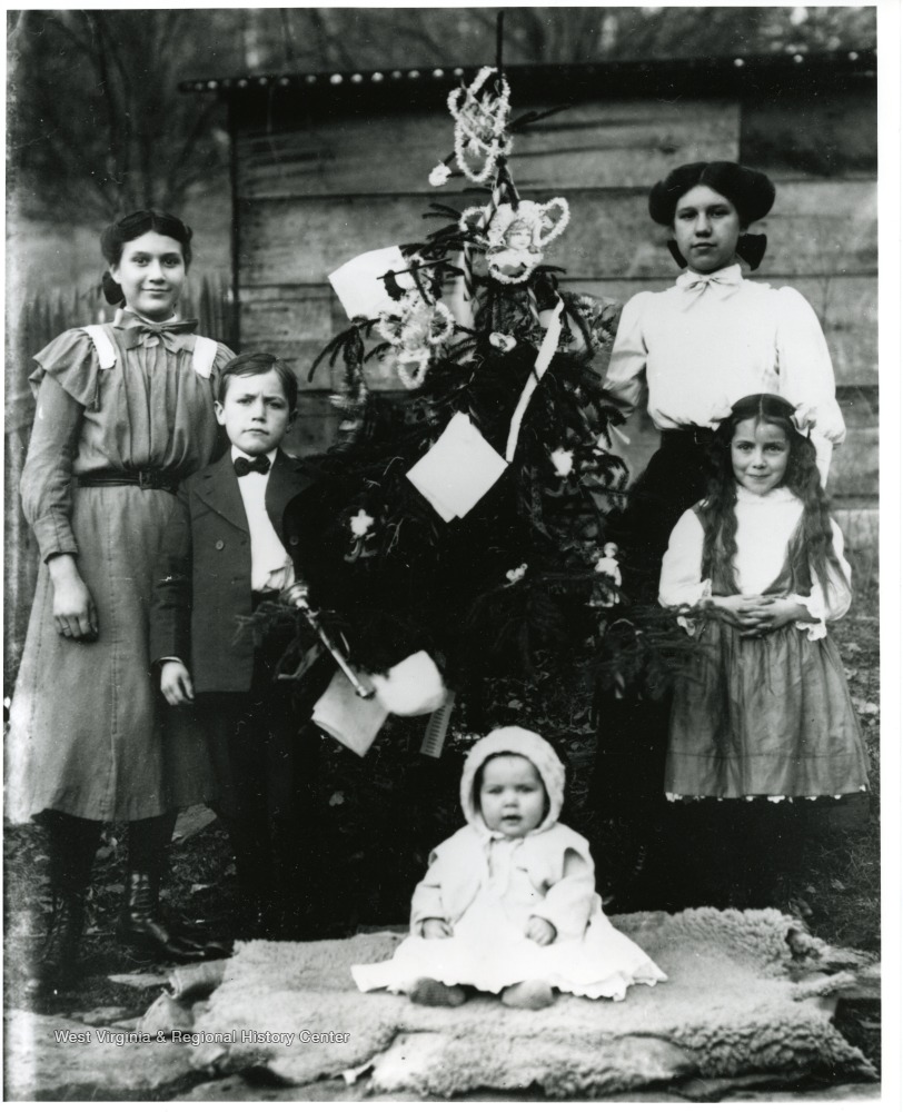 Photo of five children of various ages, arranged around a decorated Christmas tree.