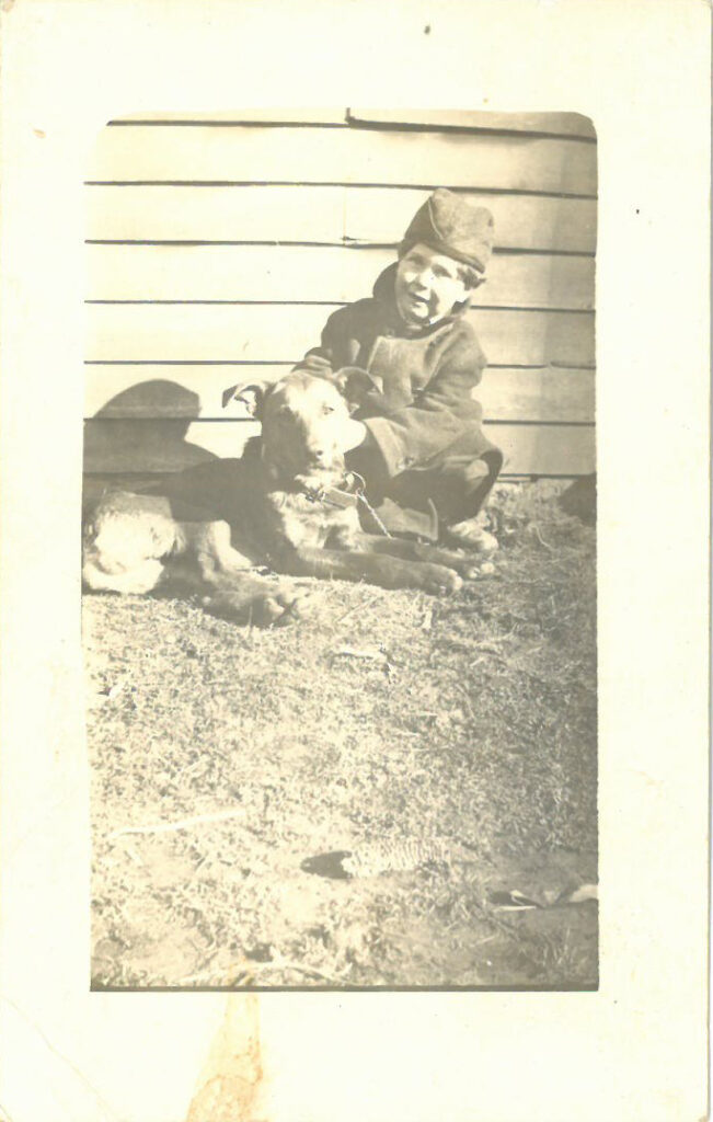 Boy seated next to dog, outside a house