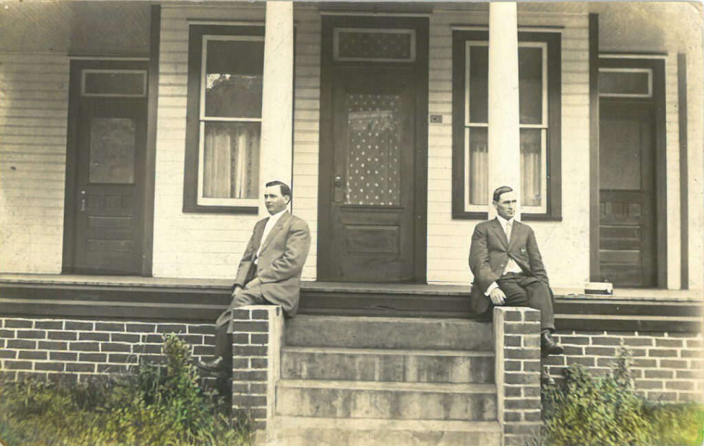 Two men seated at pillars on opposite sides of a residential front door