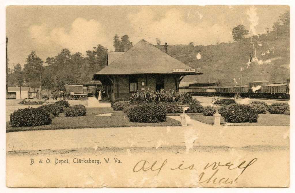 Train depot with people clustered out front, surrounded by landscaped bushes