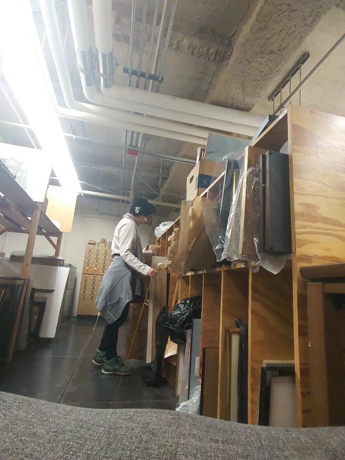 Woman standing at vertical shelves containing artwork