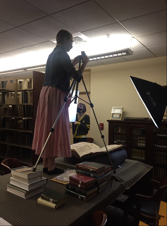 Woman operating camera on tripod to photograph a book as another woman looks on