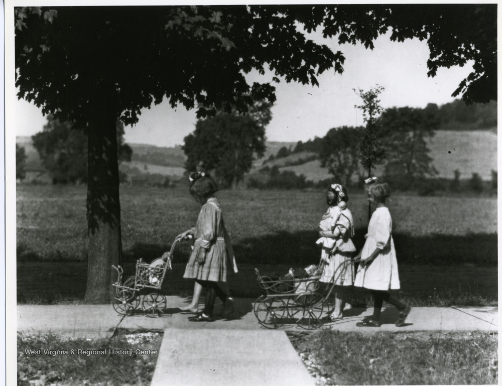 Little girls pushing dolls in prams.