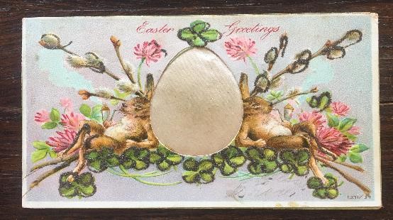 Easter postcard showing rabbits next to an egg, surrounded by greenery