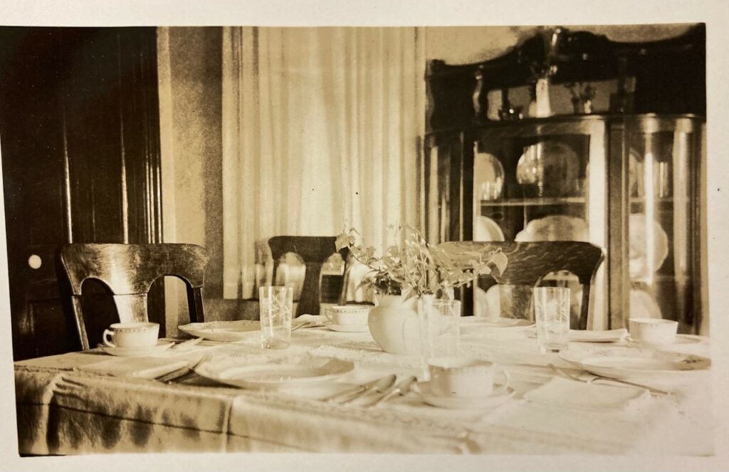 A dinner table set with china and silverware, with a tablecloth and wooden chairs.