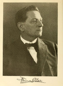 A sepia toned image of a middle aged white man in a suit jacket looking off to the side of the image. 