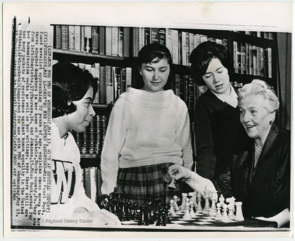 Pearl Buck, seated, with her three adopted daughters standing next to her over a chess board.