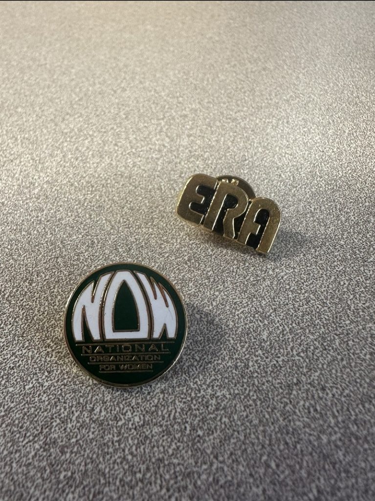 two pins, the one on the left is a circular NOW pin and the left is a gold ERA pin